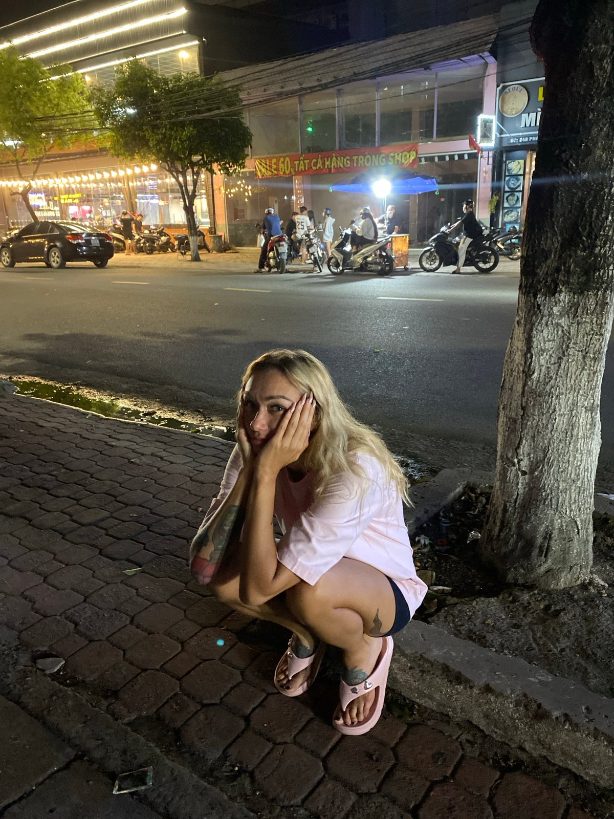 Woman crouches by tree with hands covering face in Vietnam