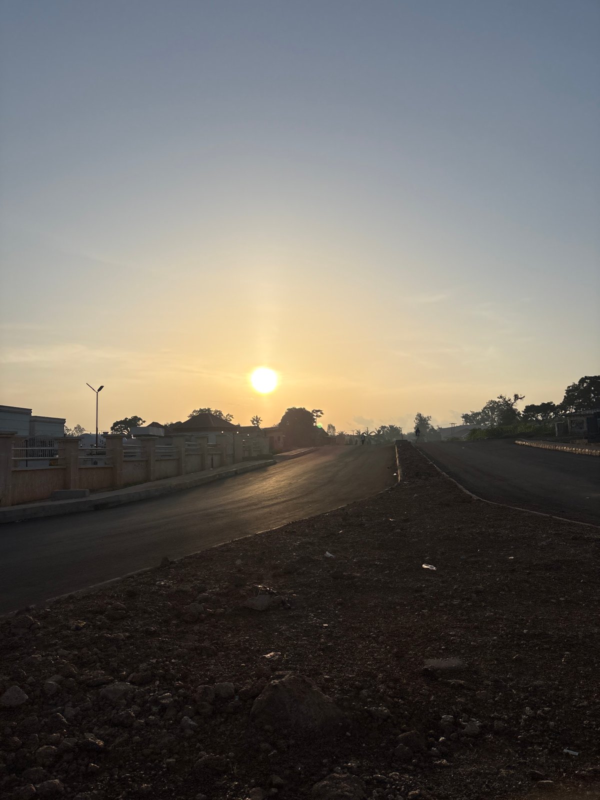 Bukuru road at sunrise, streetlights, vehicles, and low golden light