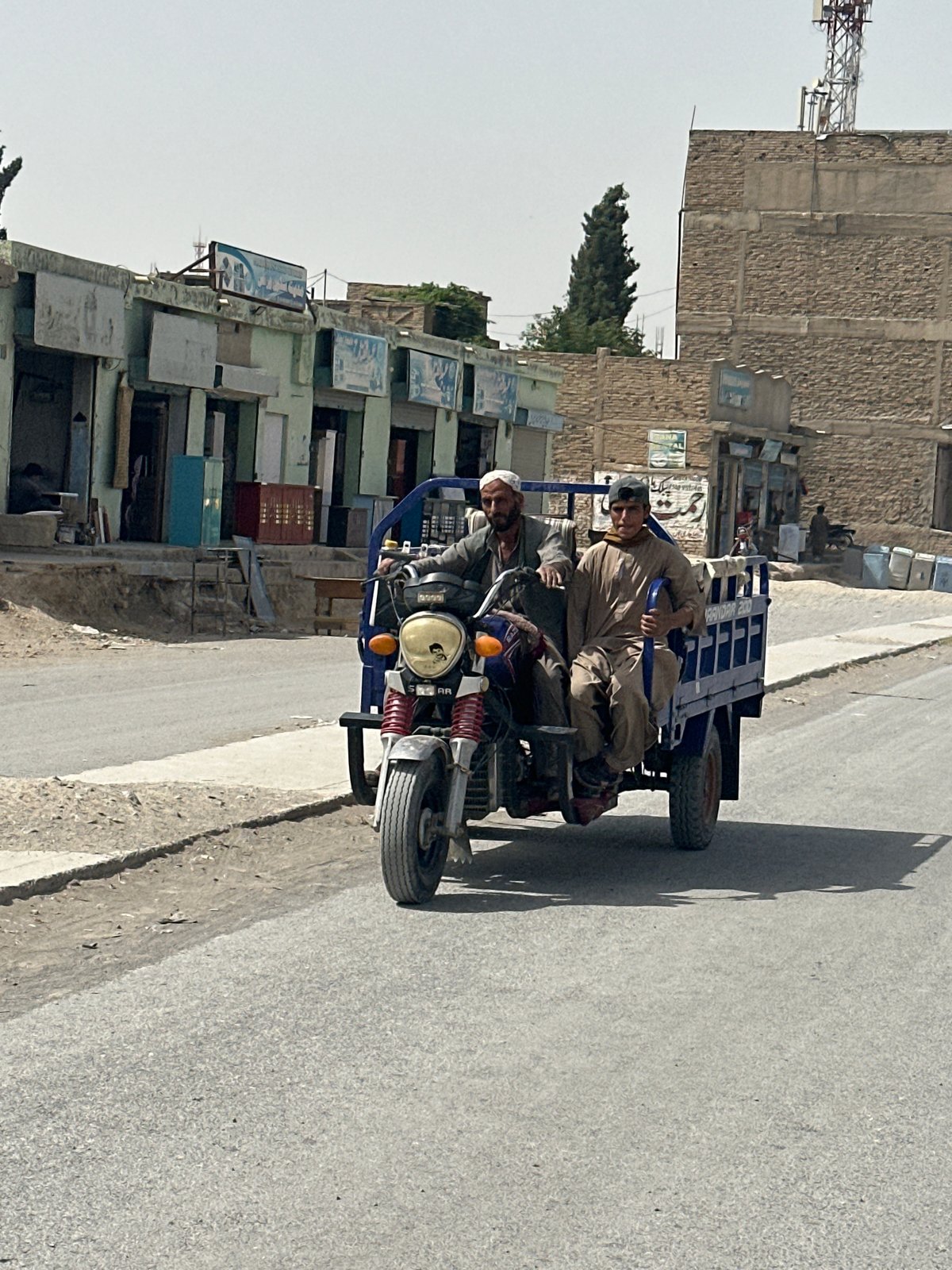 Two men ride motorcycle with trailer through Quetta streets