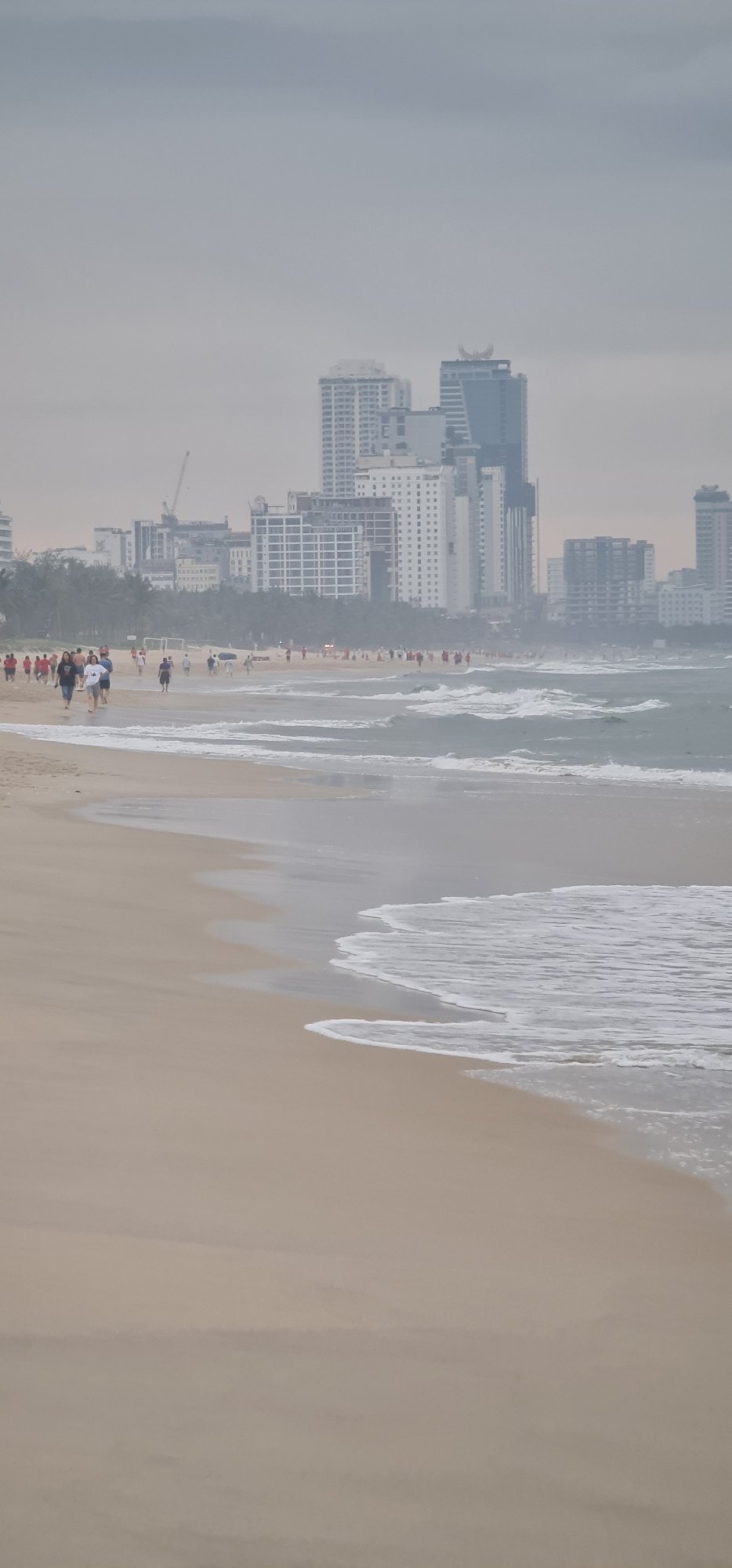 Evening beachgoers enjoy Đà Nẵng coastline under overcast skies