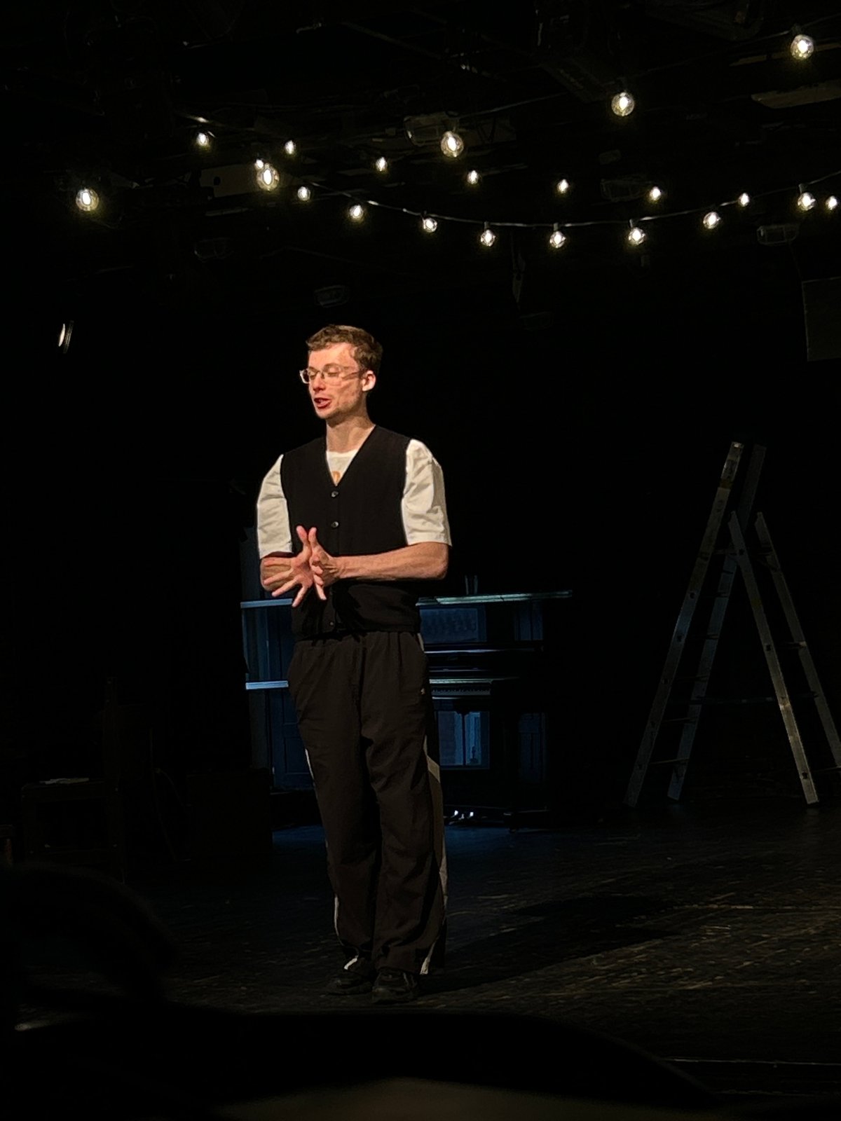 Young actor in orange sweater performs on dimly lit stage