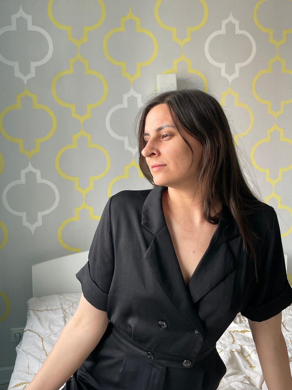 Woman in black dress documented in bedroom setting