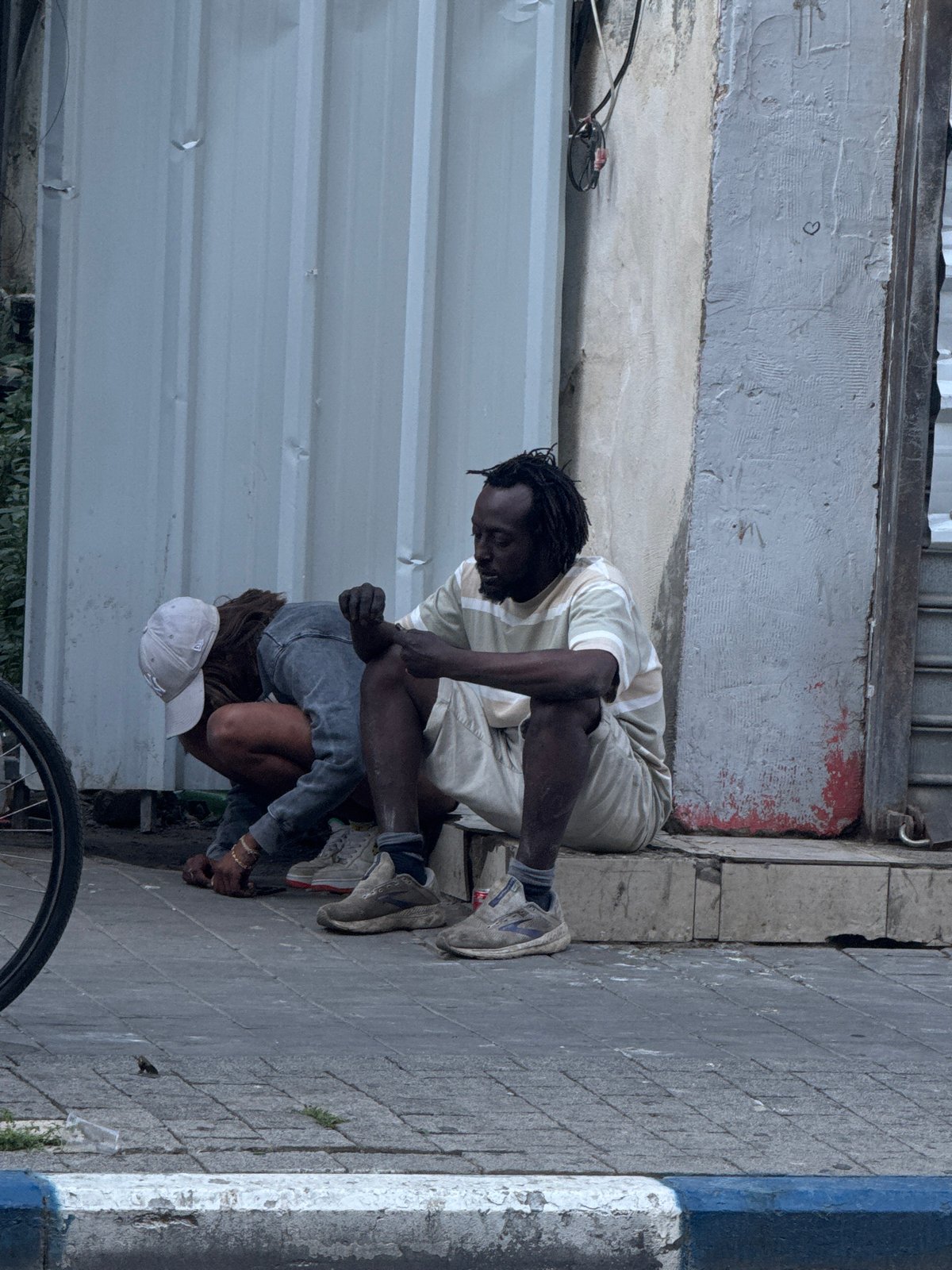 Two people crouched on Tel Aviv sidewalk early morning