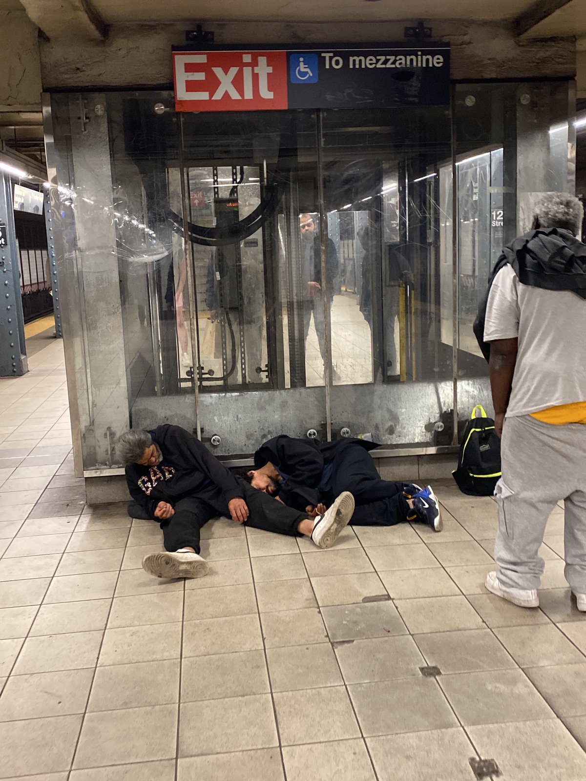 Two people sleep on subway platform floor