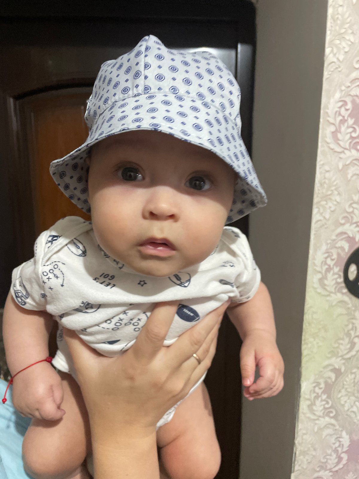 Surprised baby in bucket hat held up at home in Moldova