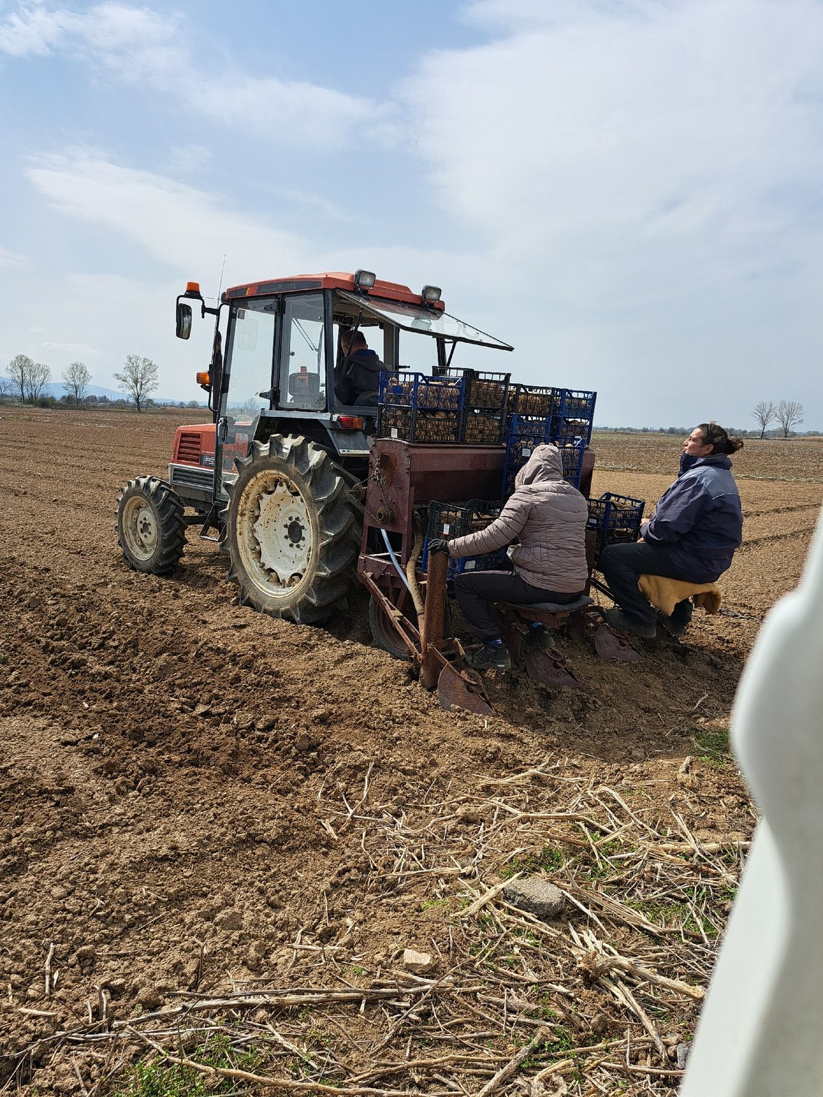 Farm workers operate equipment on red tractor in Bulgarian field