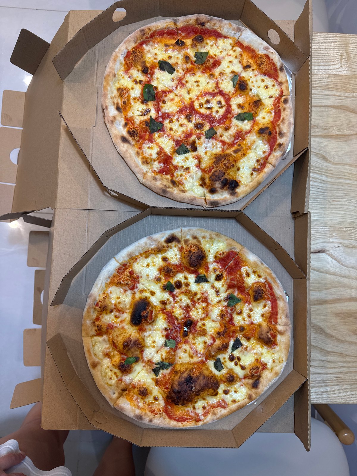 Fresh Margherita pizzas in boxes, charred crust and basil