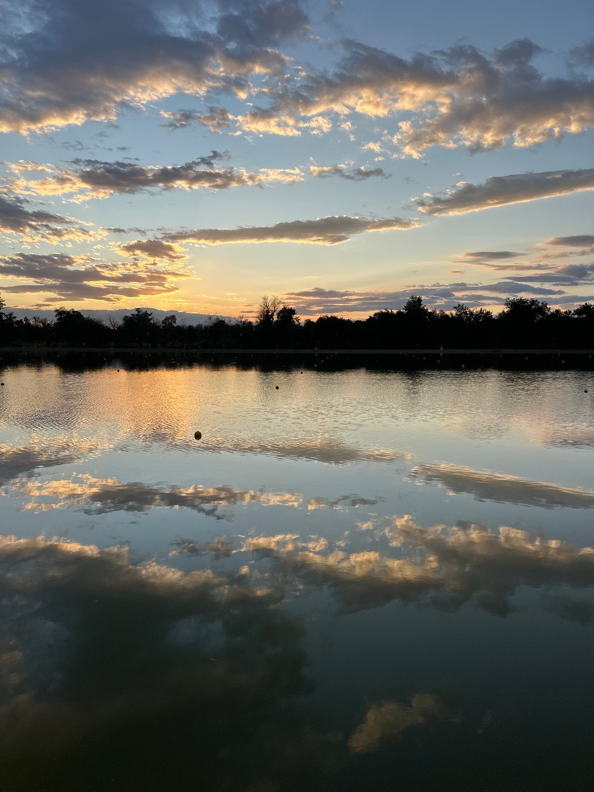 Calm lake mirrors a soft, cloudy sunset.