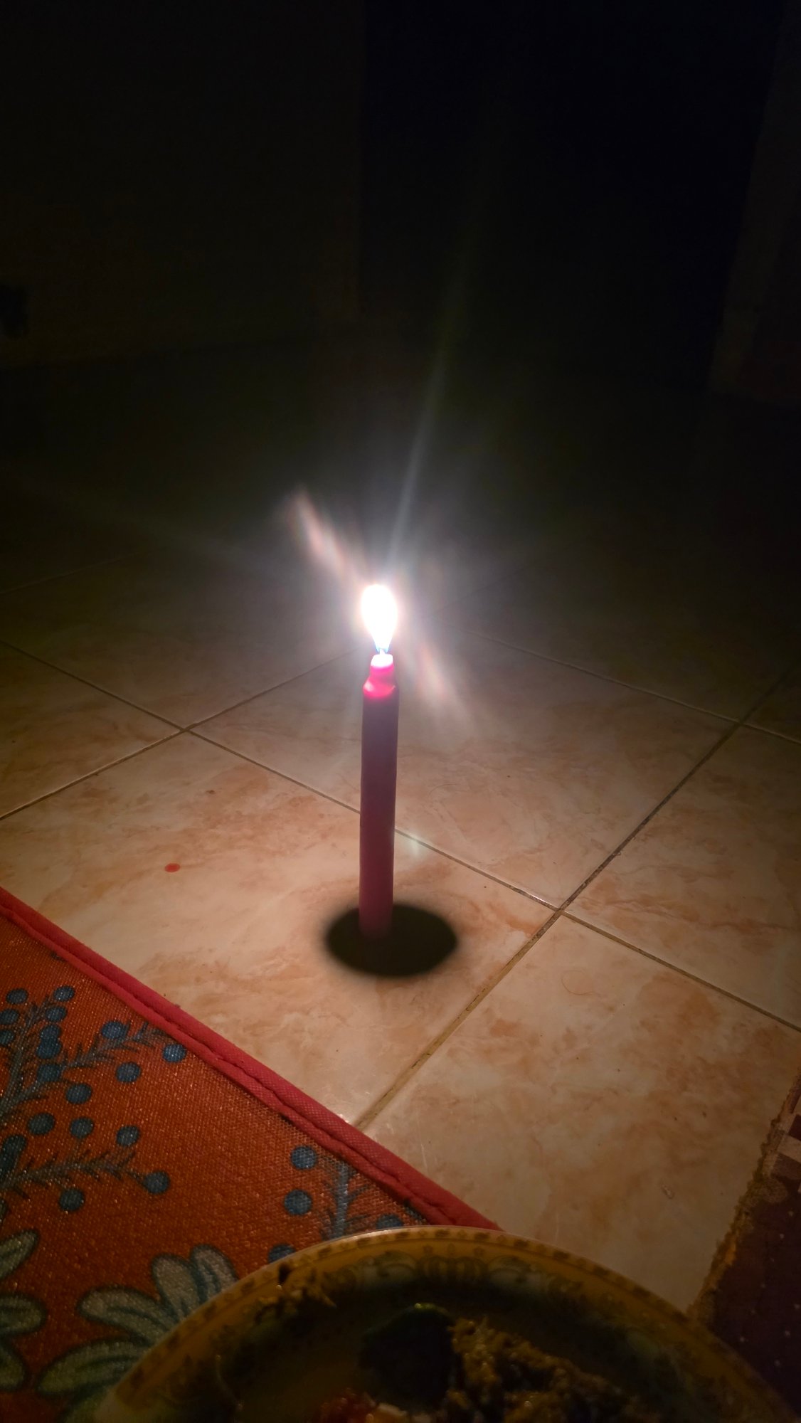 Red candle burns on tiled floor in Lhokseumawe