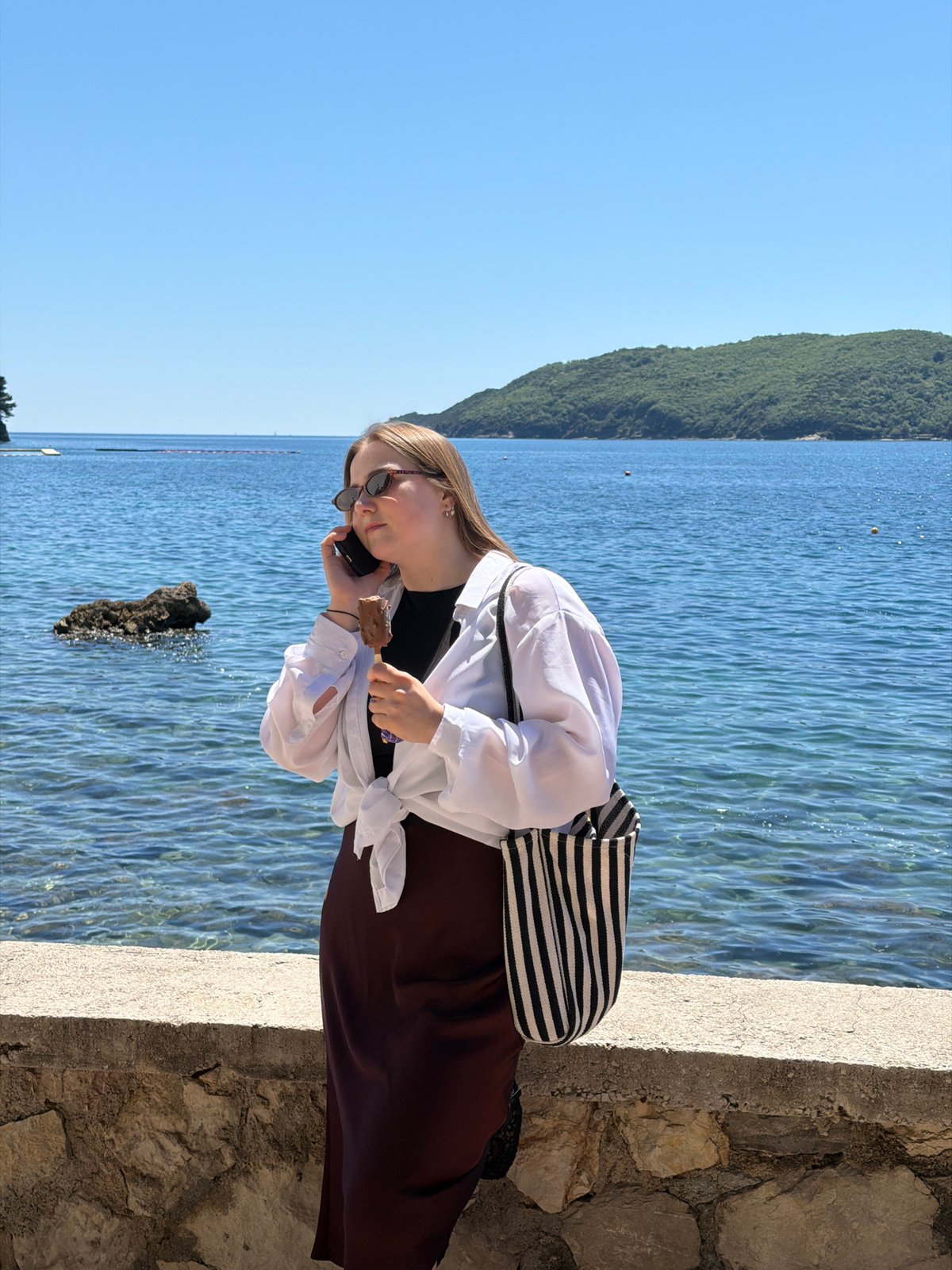 Woman enjoys phone call, ice cream at Budva seaside