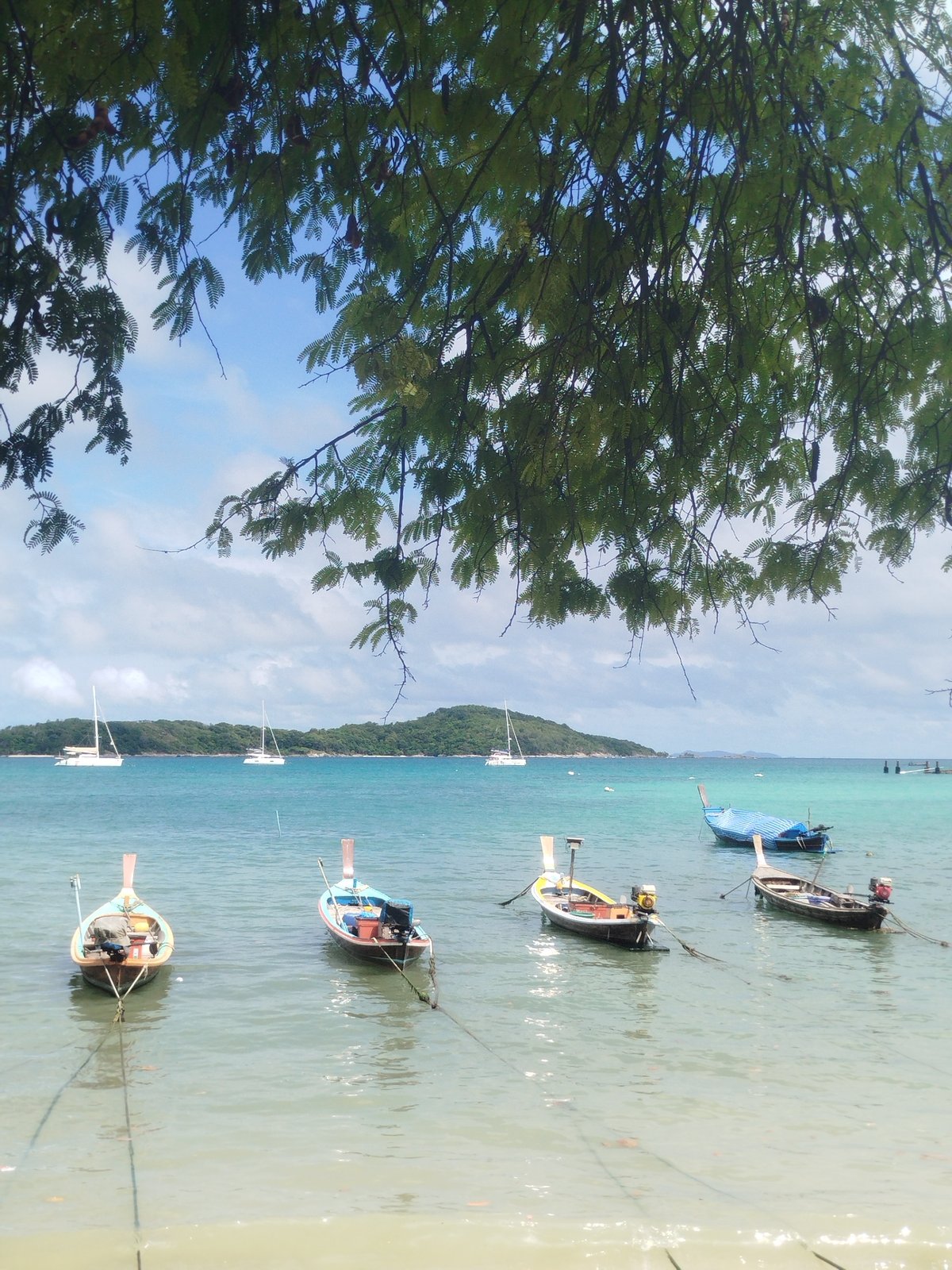 Long-tail boats rest in turquoise waters under tropical skies