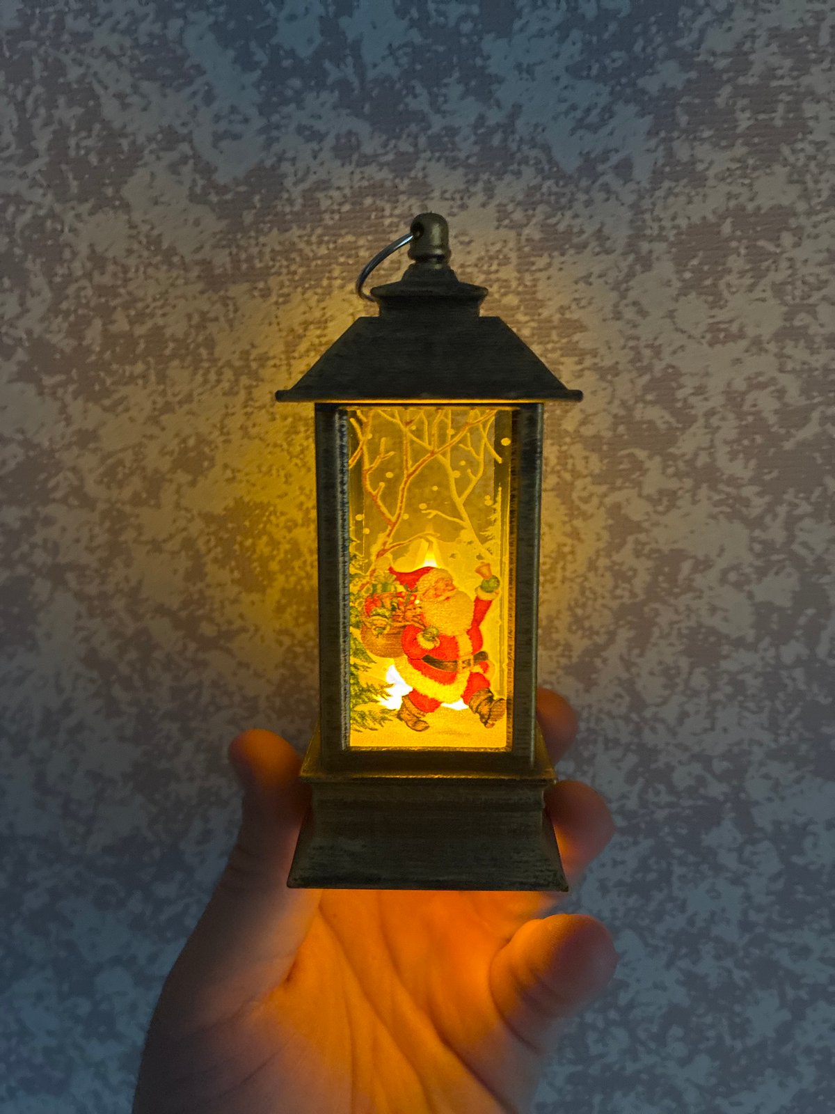 Person holds illuminated decorative lantern against textured wall