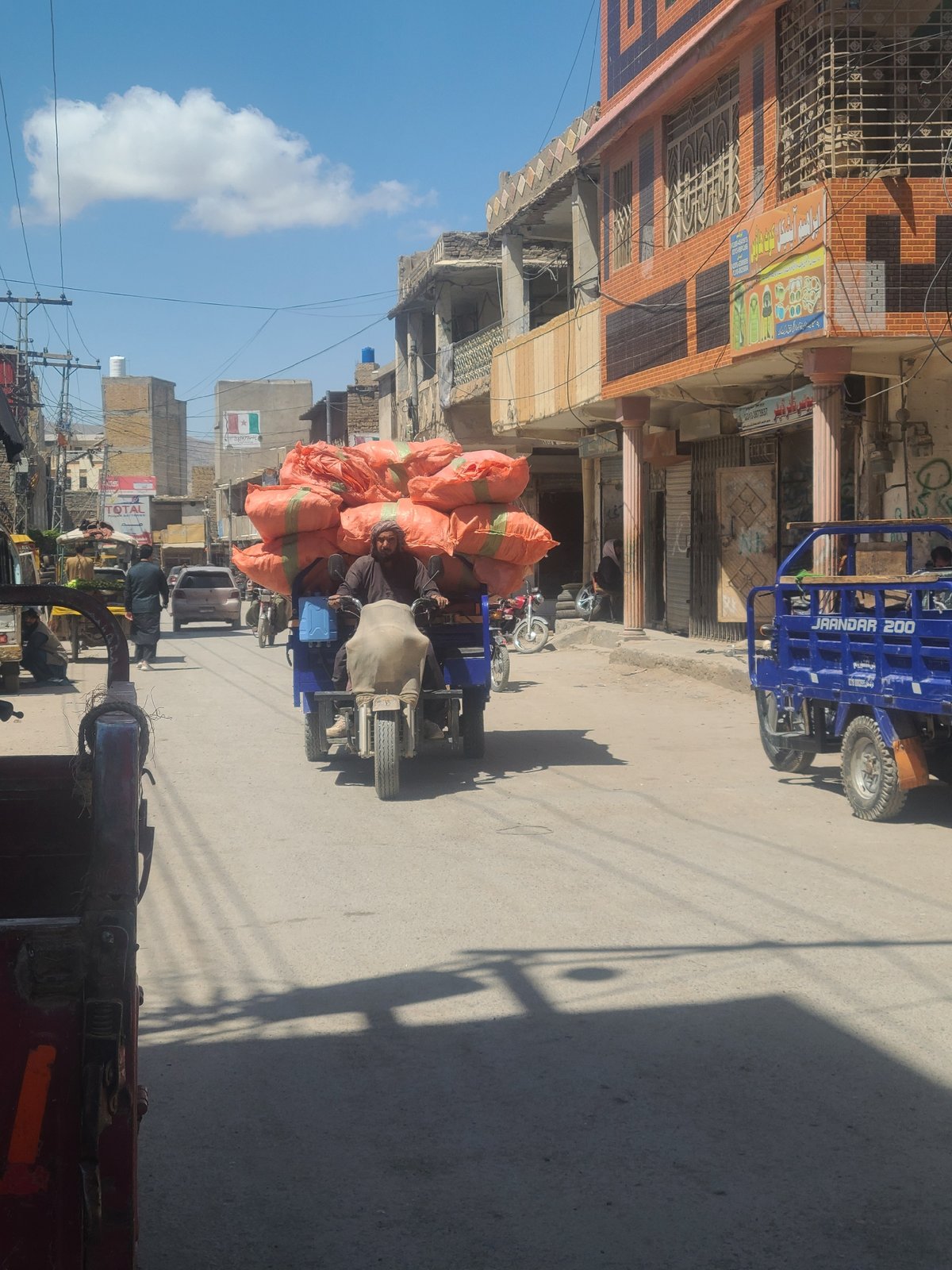 Loaded tricycle transports orange sacks through Quetta streets