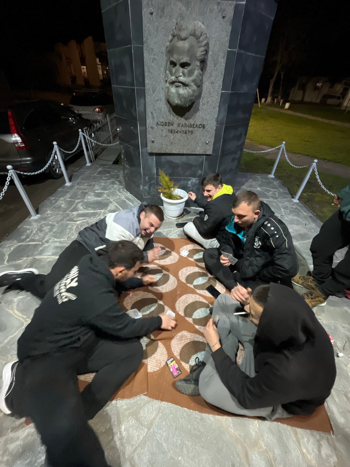 Young people play cards at Bulgarian monument at night