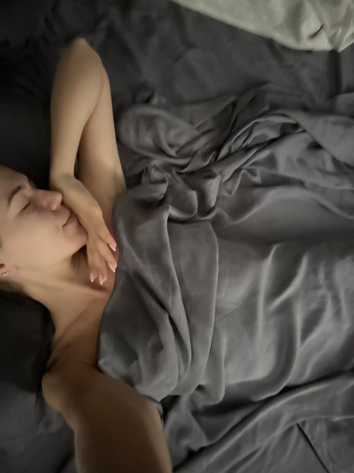 Resting in bed, grey silk sheets, eyes closed