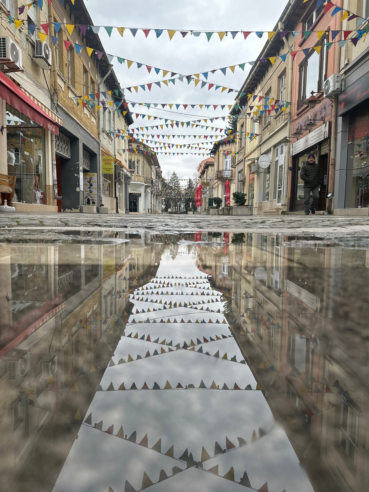 Street scene with decorative flags reflected in puddle in Vratsa