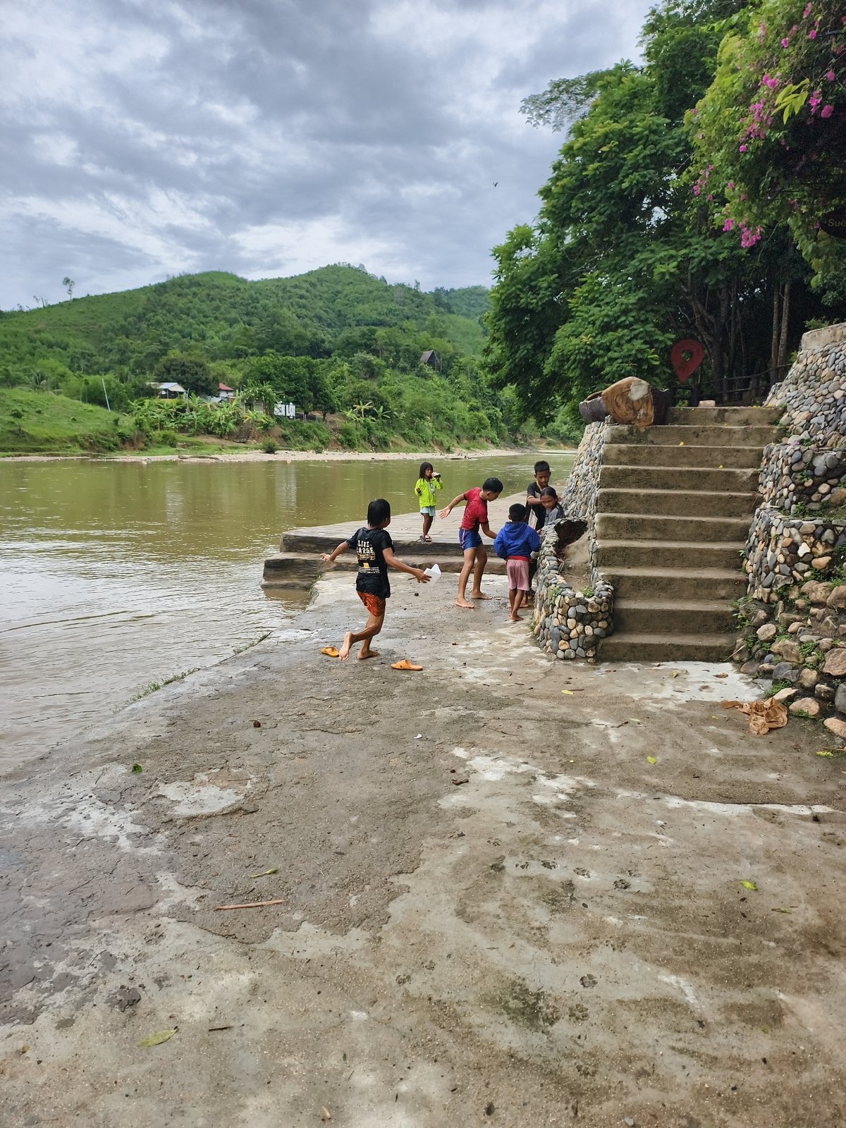 Children play by muddy river on cloudy morning