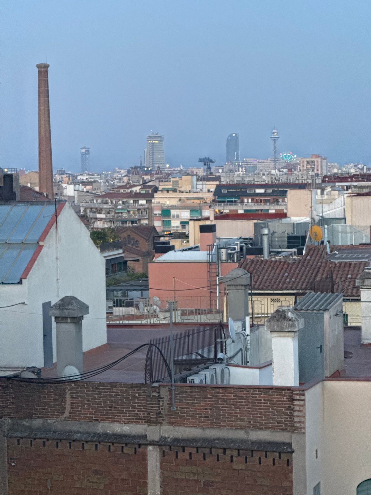 Barcelona rooftop at dusk, city sprawling under a crescent moon