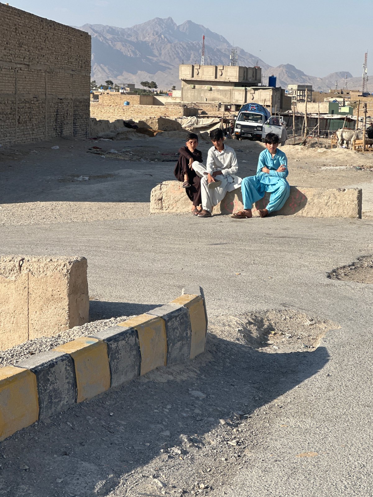 Three people on concrete barrier in dusty Quetta streets