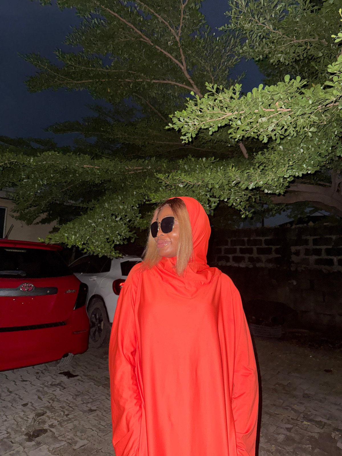 Night poses in orange near parked cars, Ado Nigeria