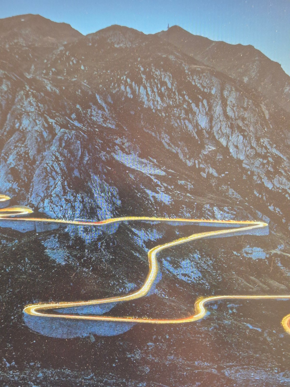 Light trails curve through a dramatic mountain road at night