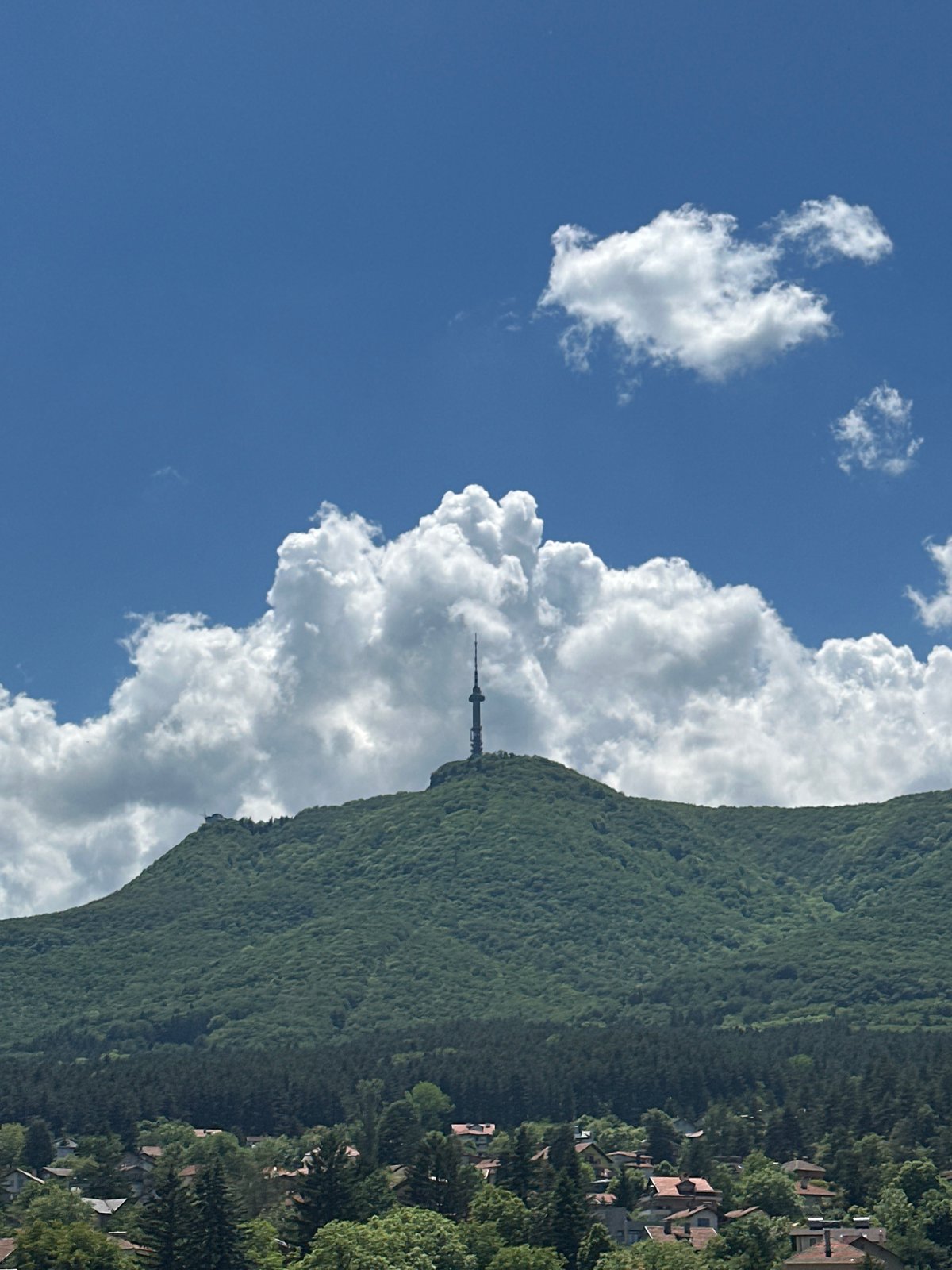 Communication tower observed on verdant mountainside under cloudy skies