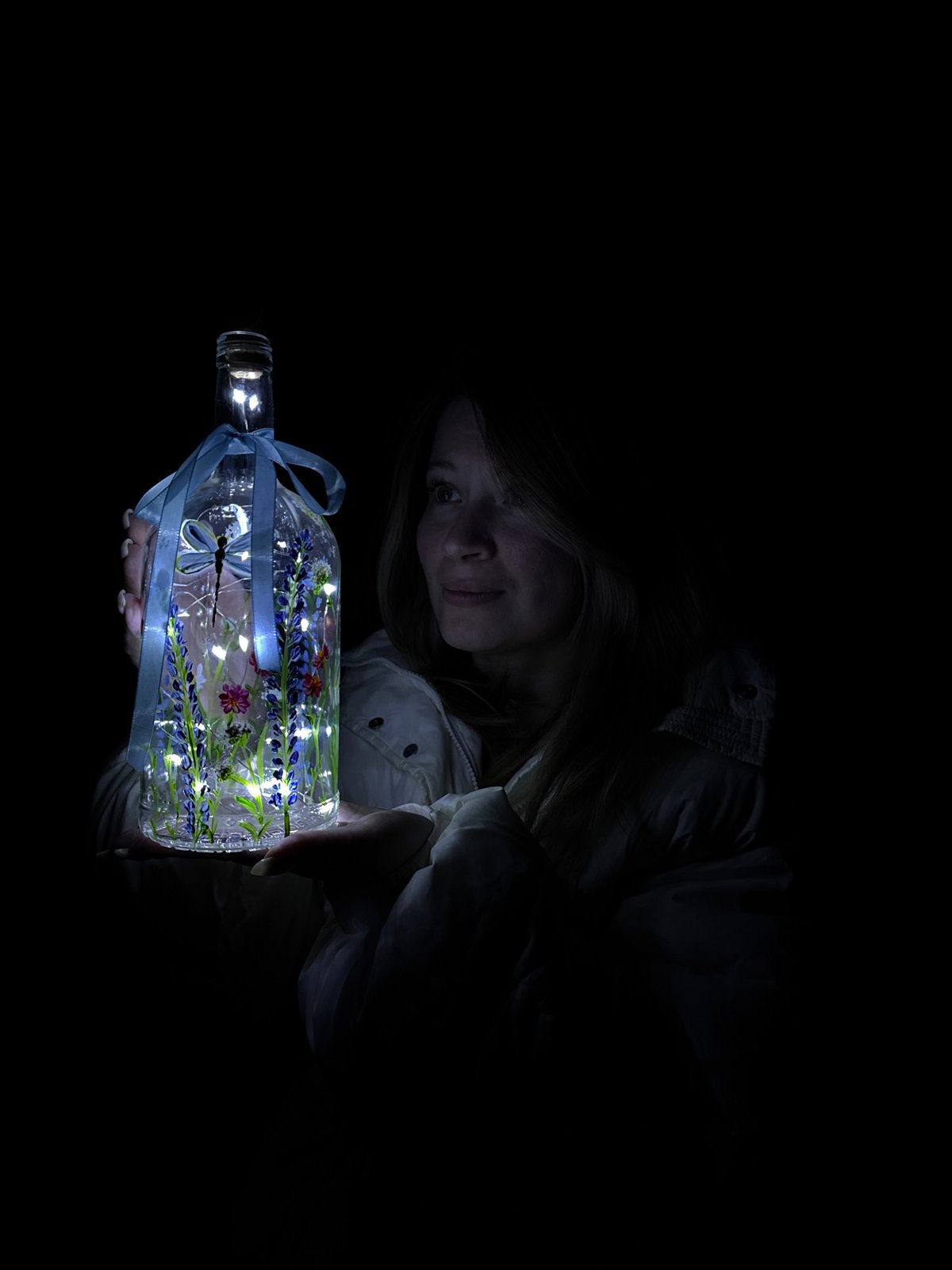 Woman poses with illuminated decorative bottle in Russian village