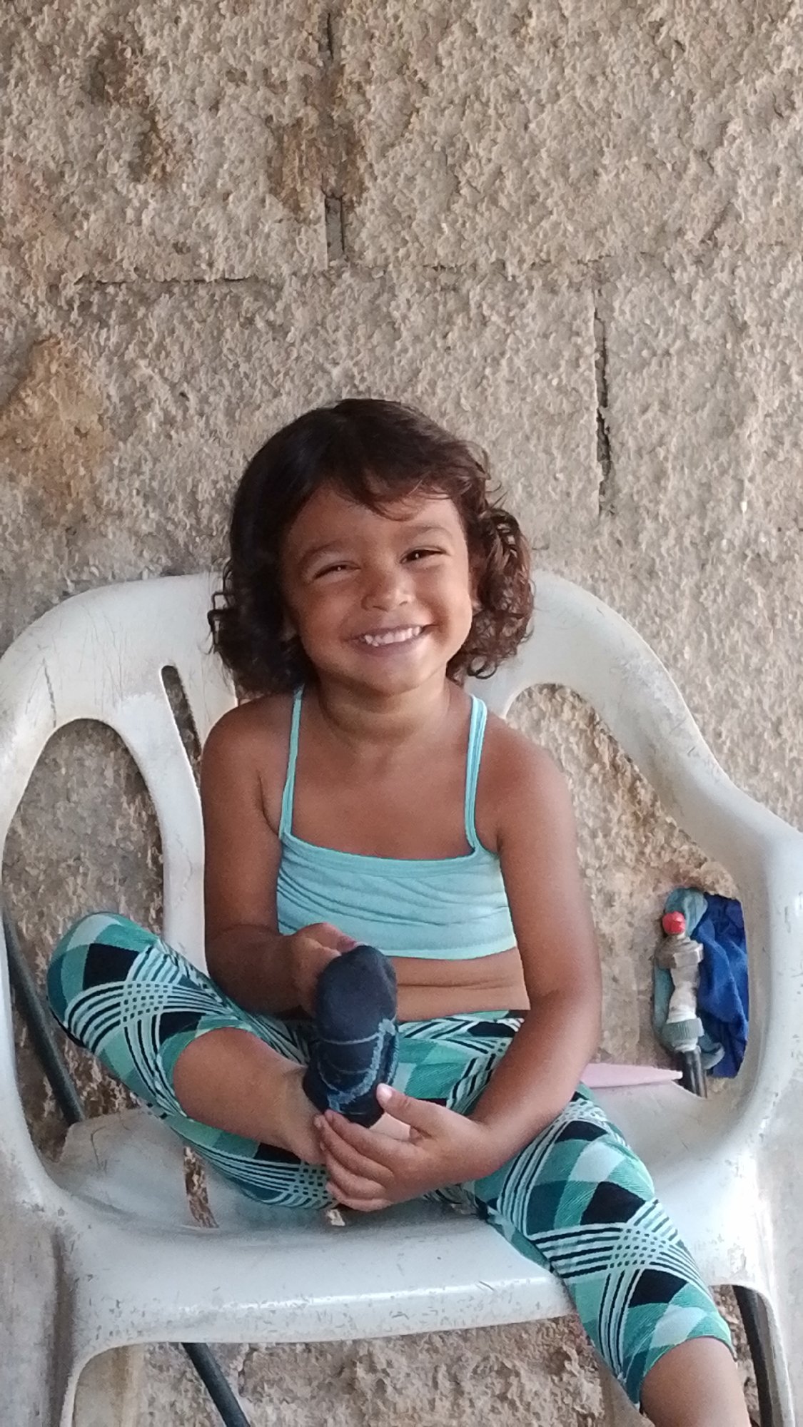 Young girl sits smiling with sock in Tinaquillo home