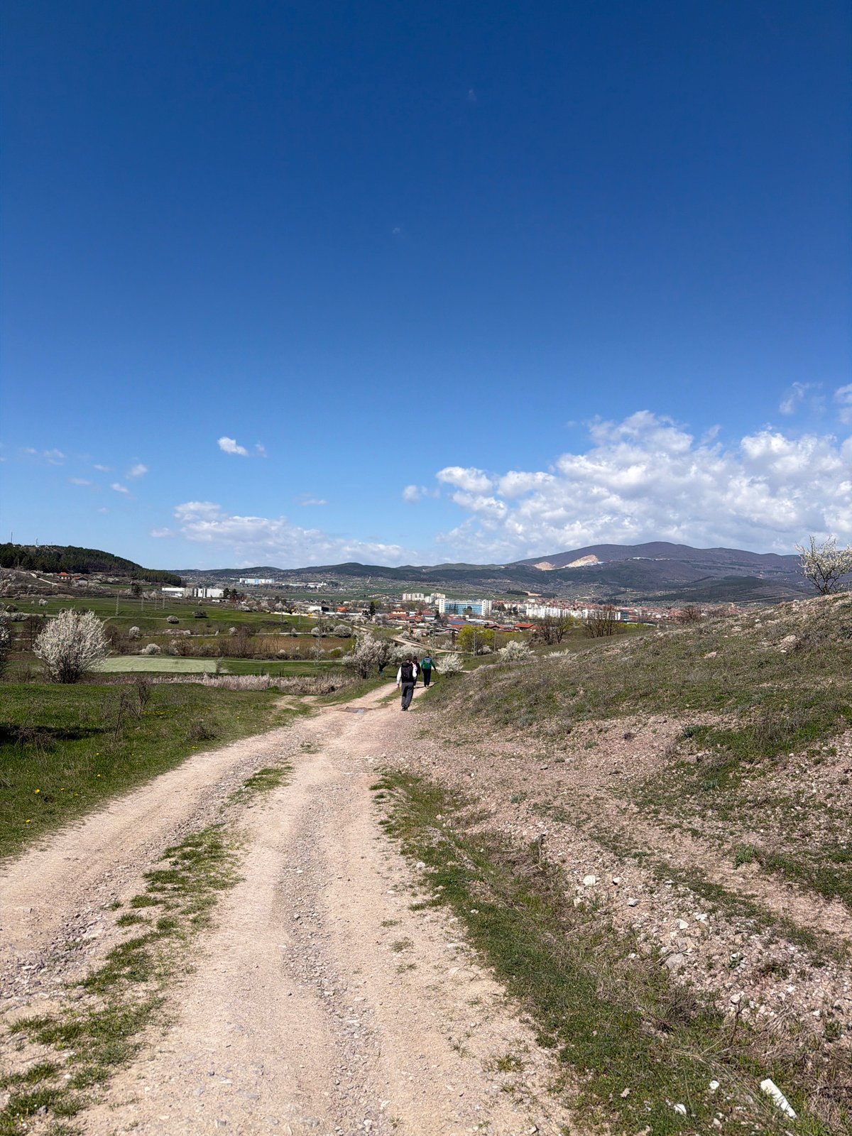 People walk dirt road near Panagyurishte on sunny spring morning