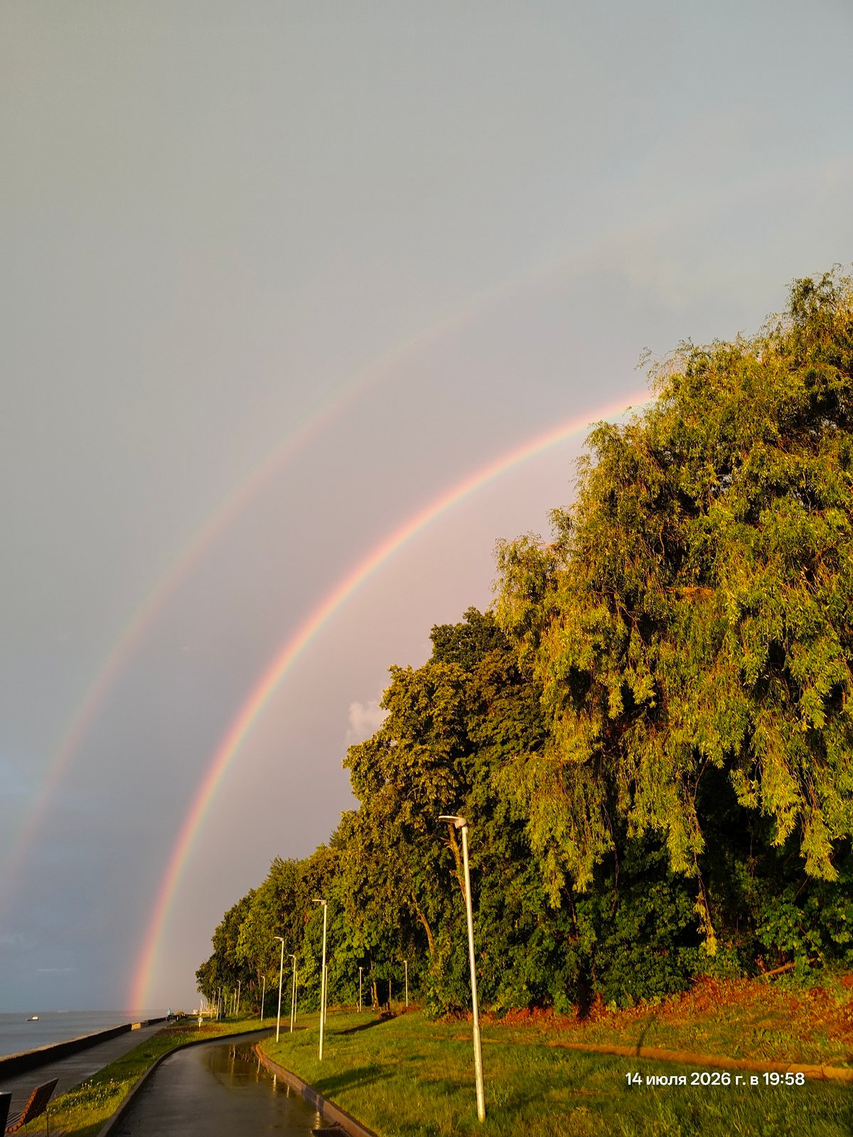 Double rainbow over a wet waterfront promenade at sunset