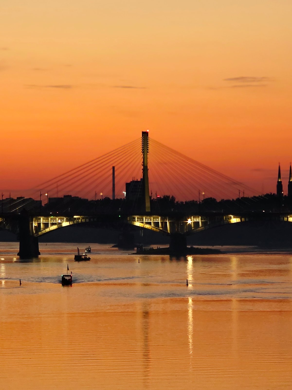 Warsaw's Vistula riverfront at golden hour, bridges and stadium lit up