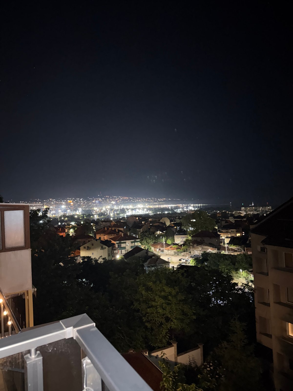 Nighttime cityscape views captured from balcony with cocktail bottle