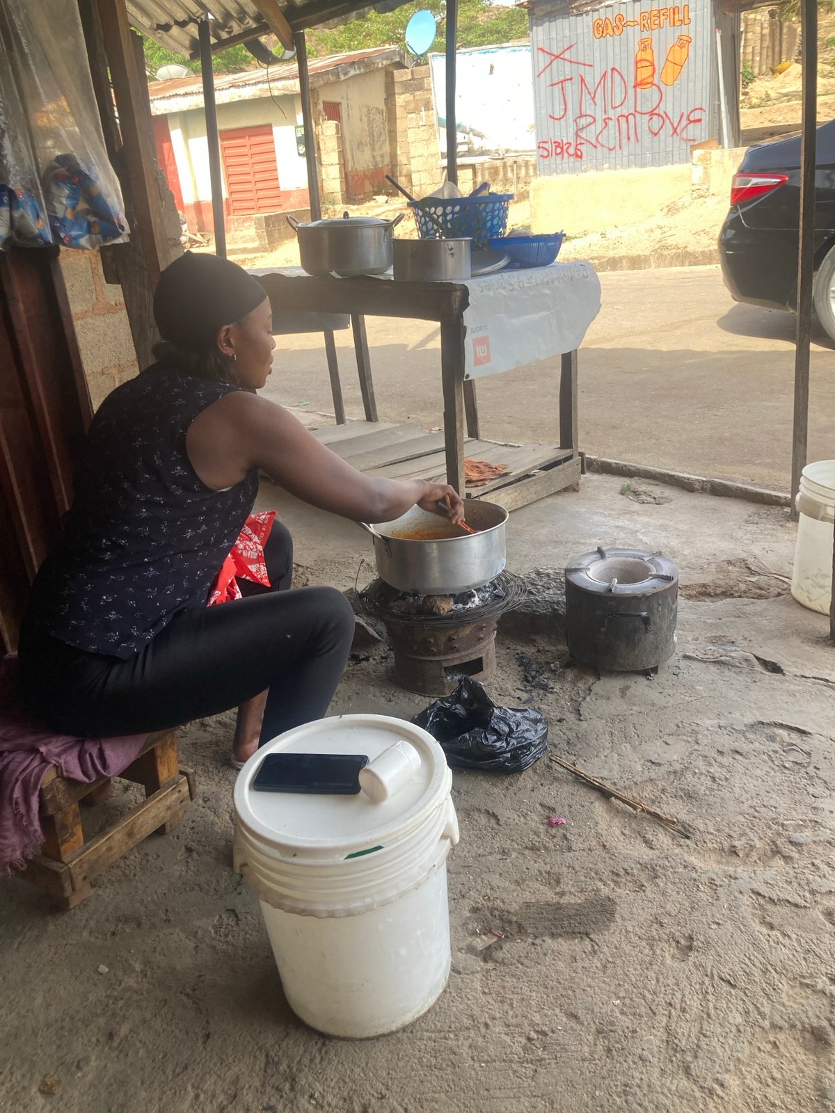 Person cooks outdoors on wooden pallet in Jos, Nigeria