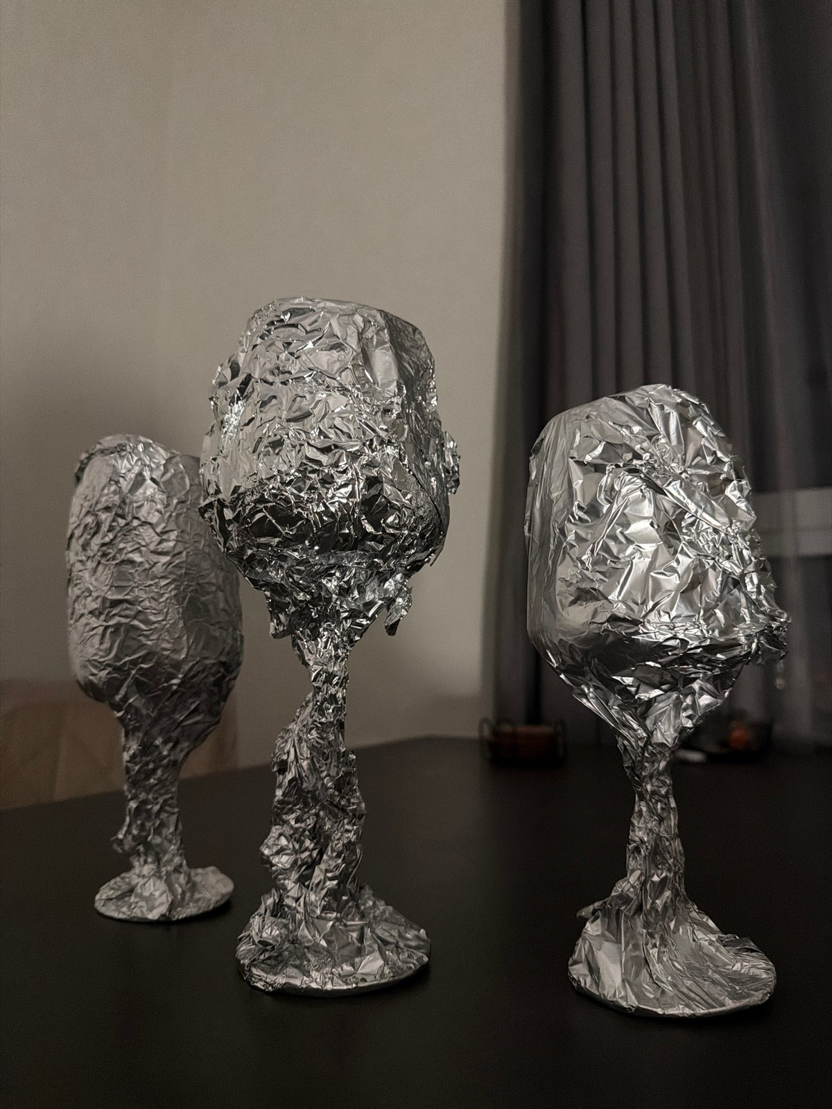 Person wraps wine glasses in foil, cat investigates