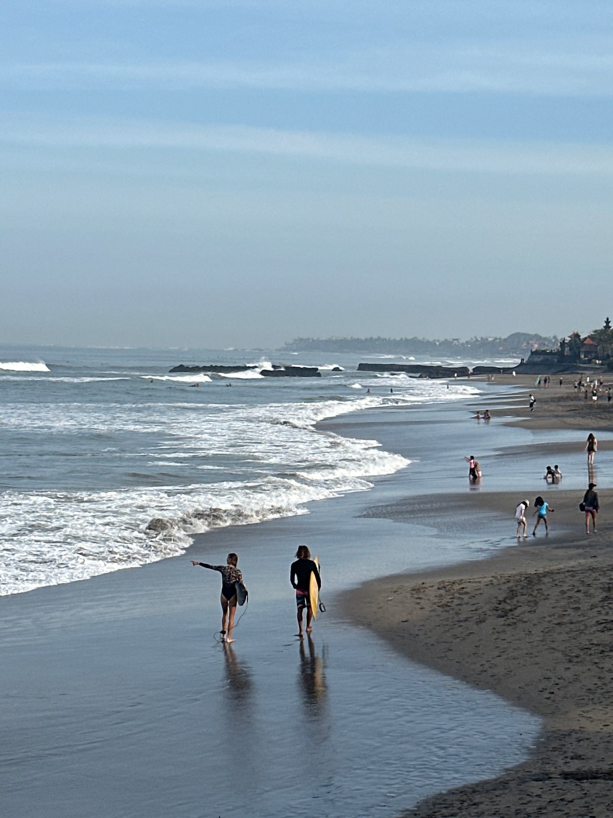 Surfers and beachgoers on North Kuta's dark sand shore