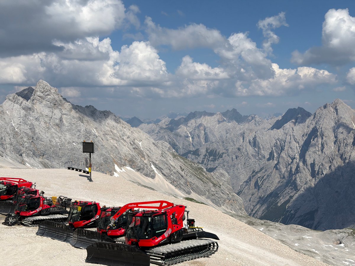Red snow groomers parked against Garmisch's rocky alpine peaks