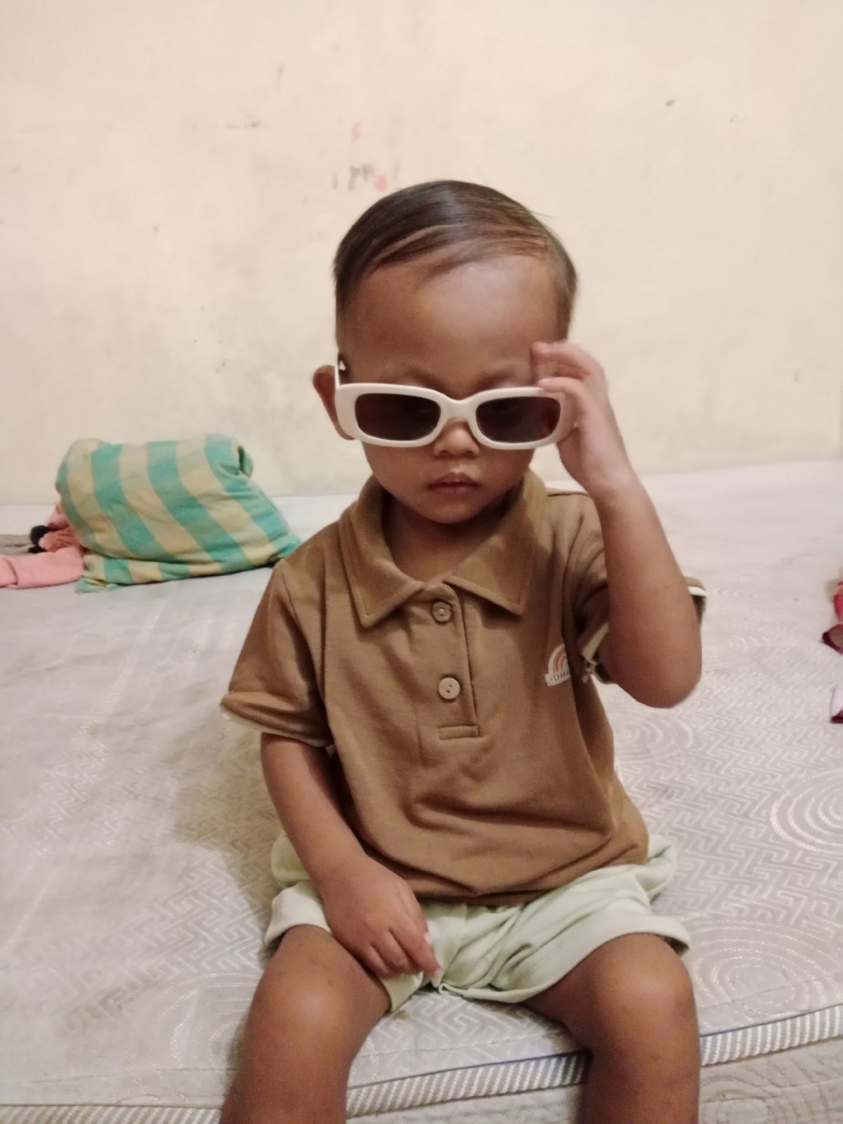 Oversized sunglasses and a raised hand on a mattress in Pati