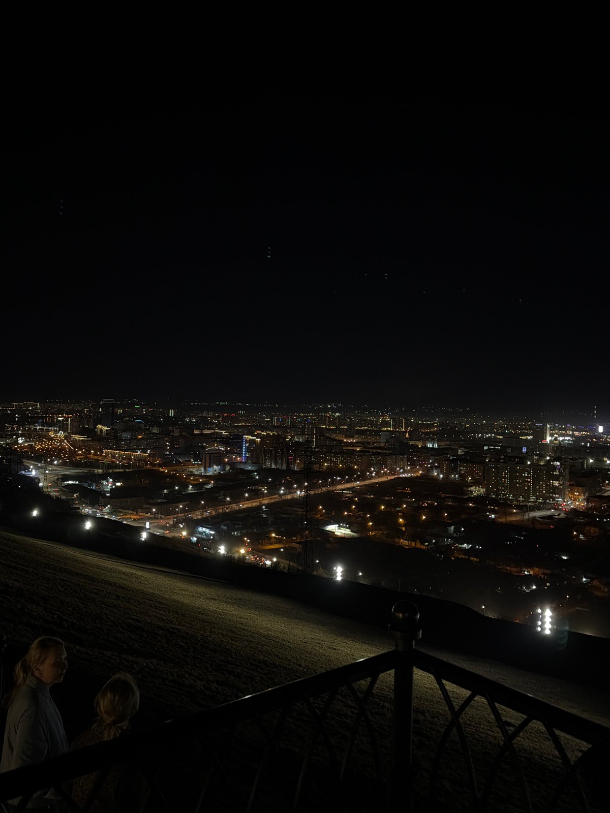 Nighttime gathering at illuminated Krasnoyarsk chapel with fireworks, city views