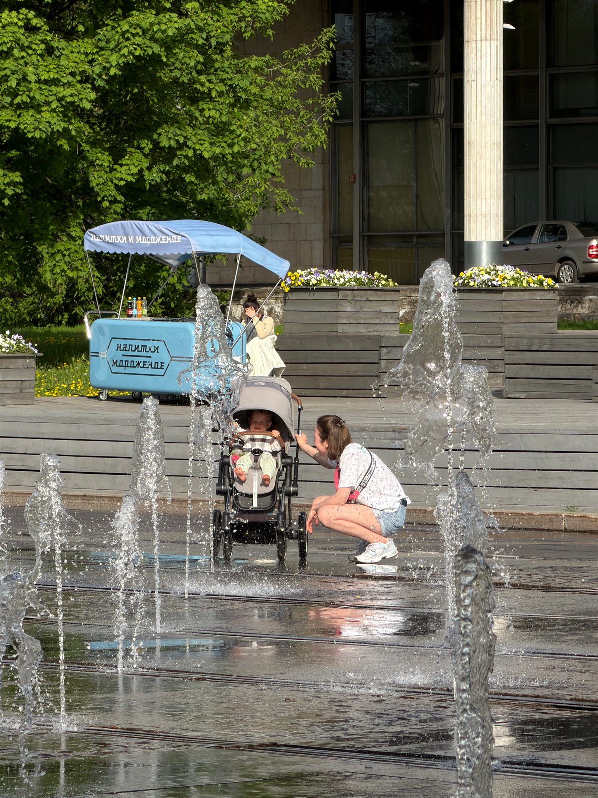 Woman with stroller pauses at Moscow fountain near beverage stand