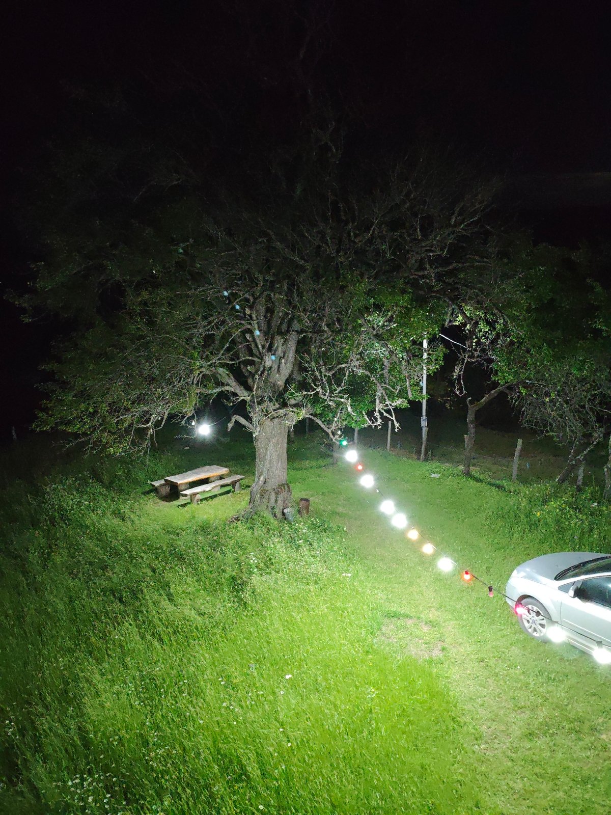 Lit outdoor space at night with parked car and picnic area