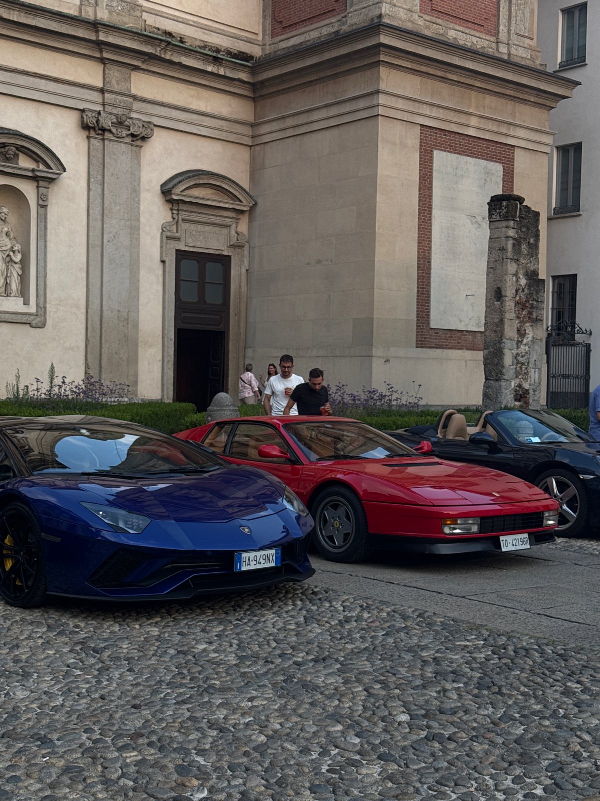 Luxury cars gather on cobblestones outside a Milan church