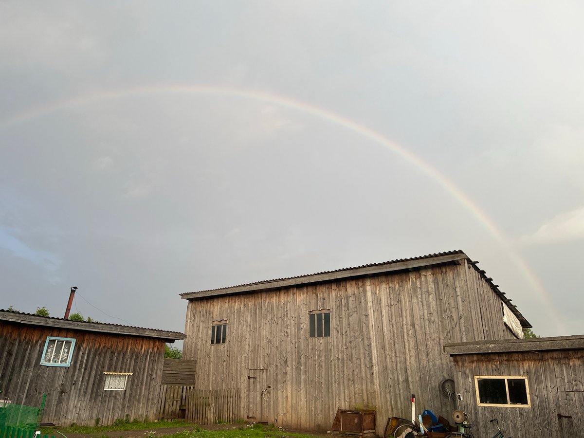Rainbow appears over wooden buildings in rural Russia