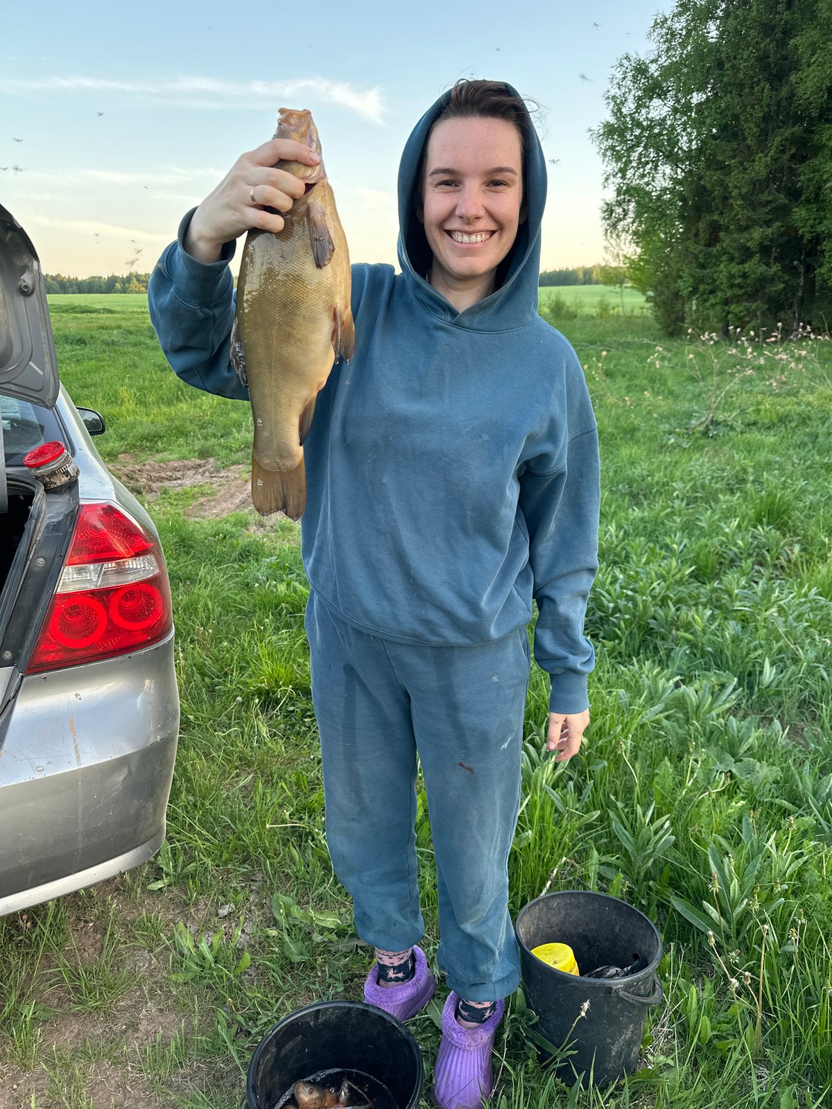 Woman displays large tench fish beside car in Russian field