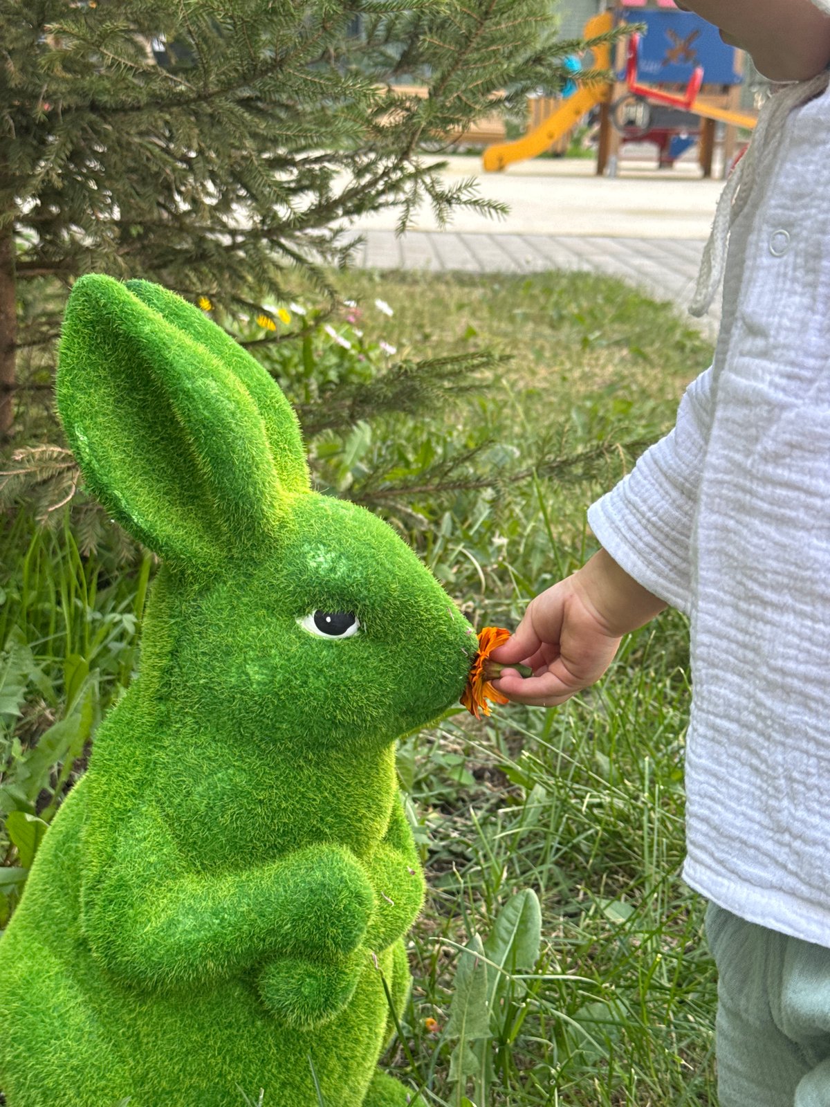 Child plays with green topiary rabbit in Moscow park