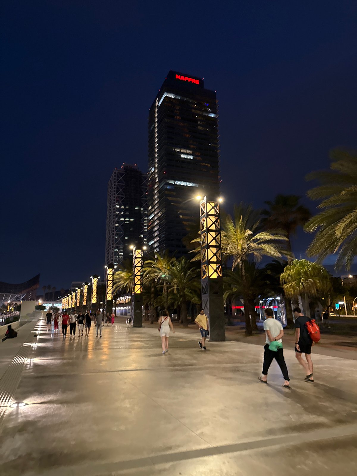Evening crowds stroll Barcelona's lit beachfront promenade