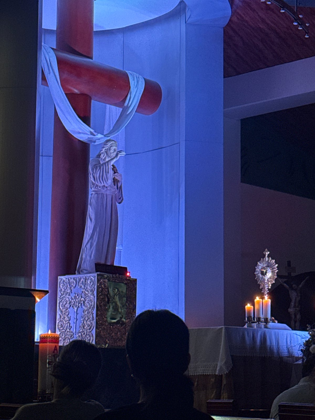 Nighttime religious scene with red crucifix and white statue documented