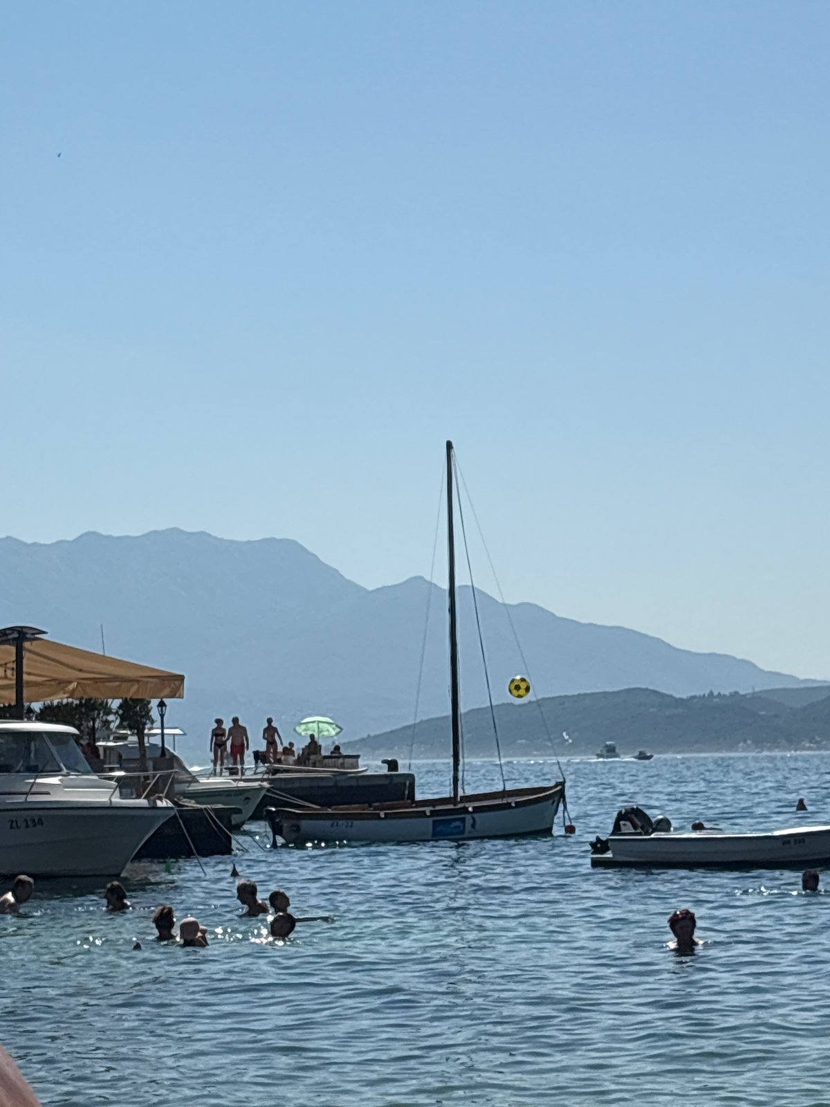 Clear water, boats, and forested cliffs at Đenovići beach