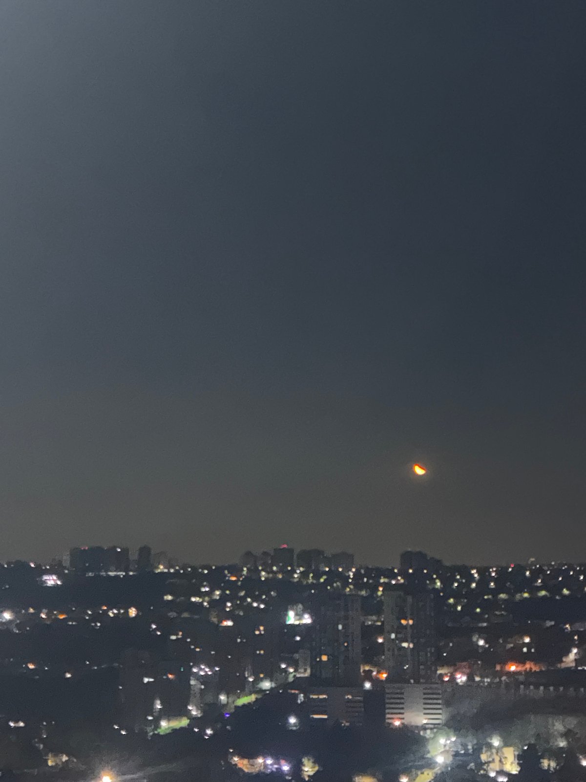 Crescent moon visible over illuminated Huixquilucan cityscape at night