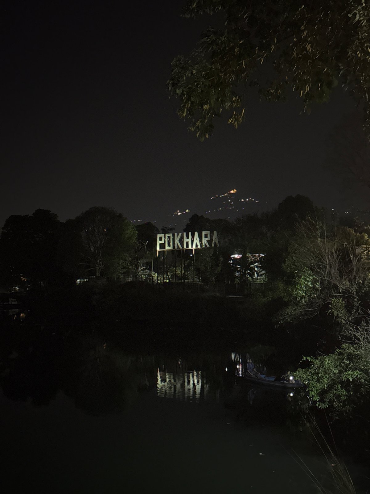 Illuminated POKHARA sign reflects in water at night