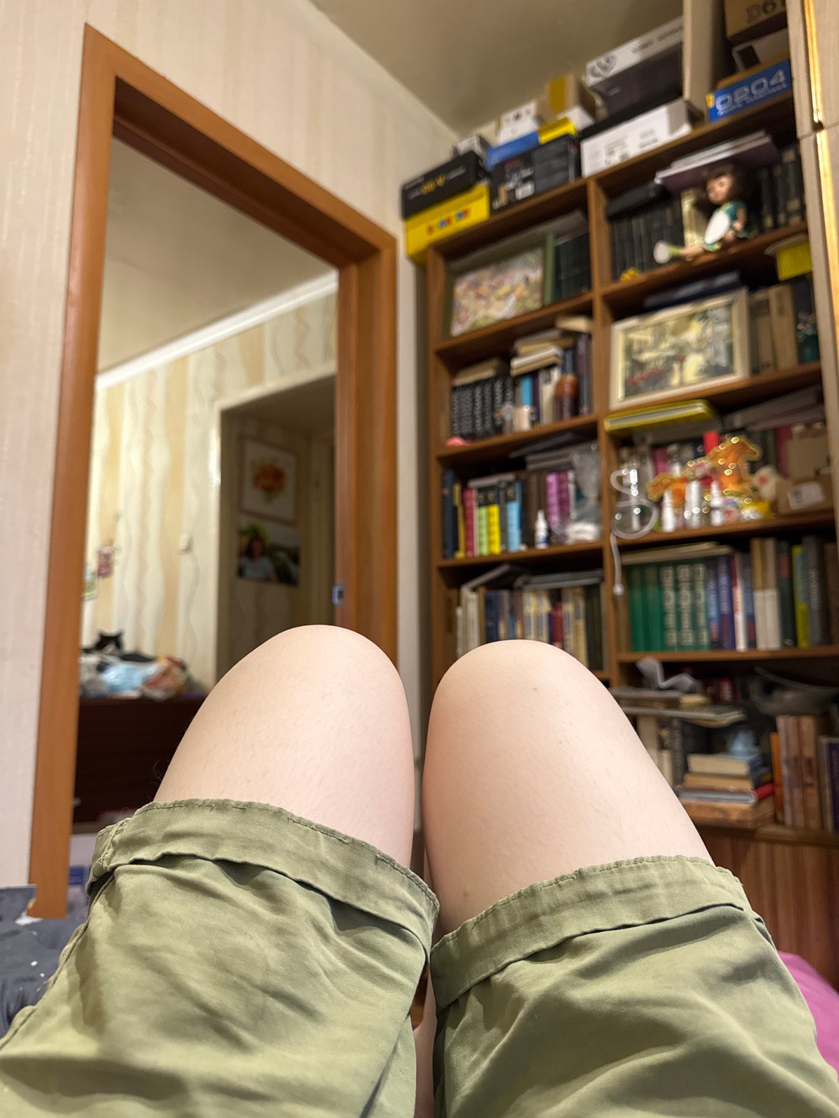 Person in green shorts photographed near bookcase in Izhevsk